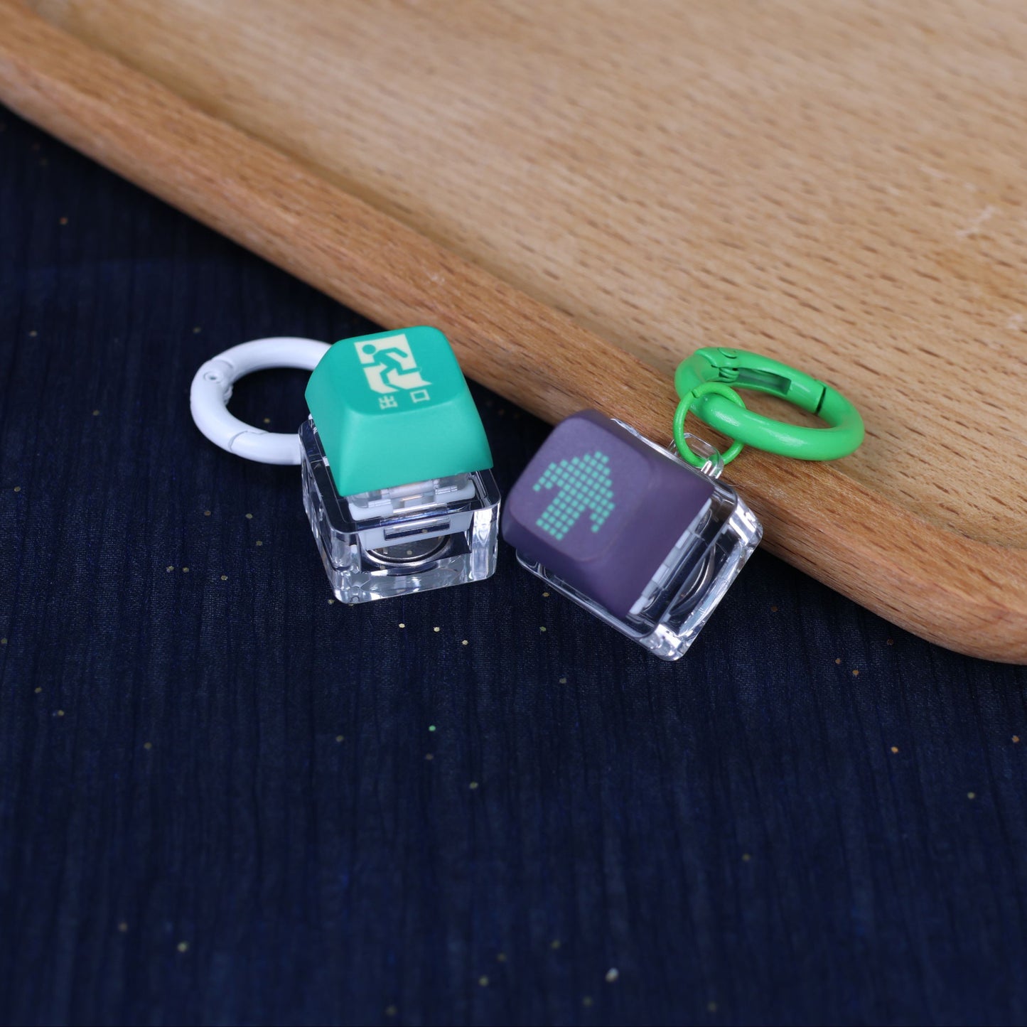 Two small electronic devices with green and black keycaps on a wooden surface.