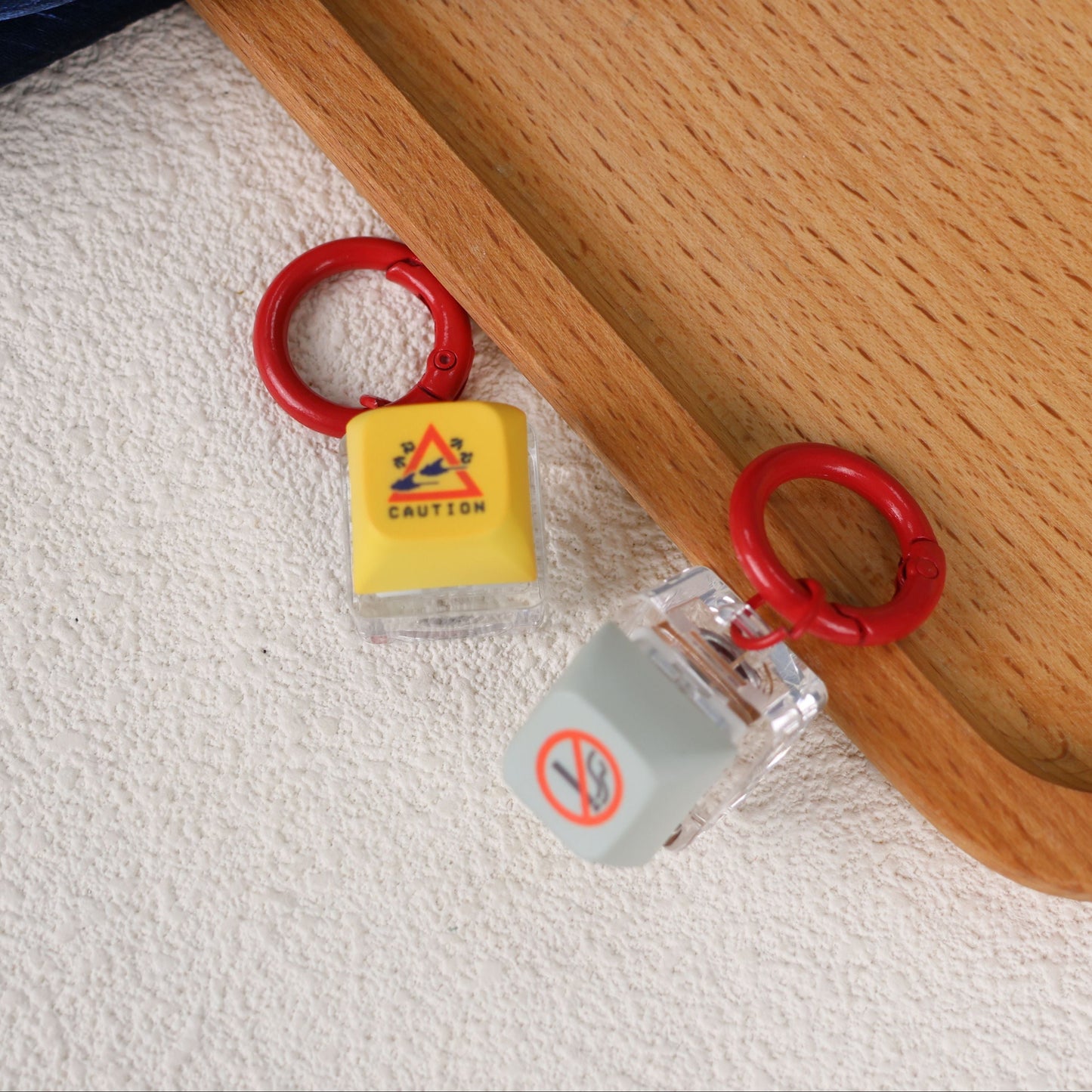 Two yellow and grey keycaps with red loops on a wooden surface