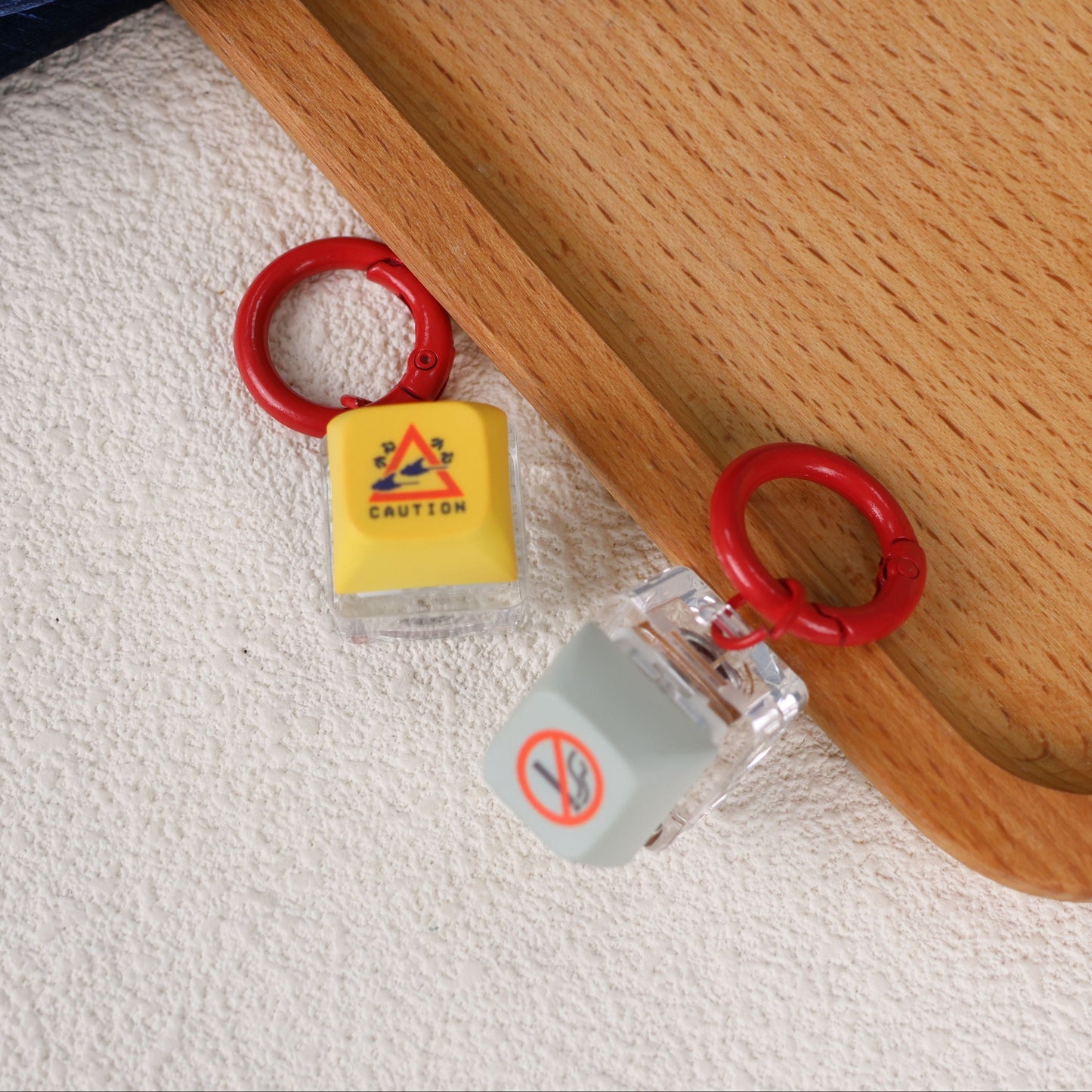 Two yellow and grey keycaps with red loops on a wooden surface