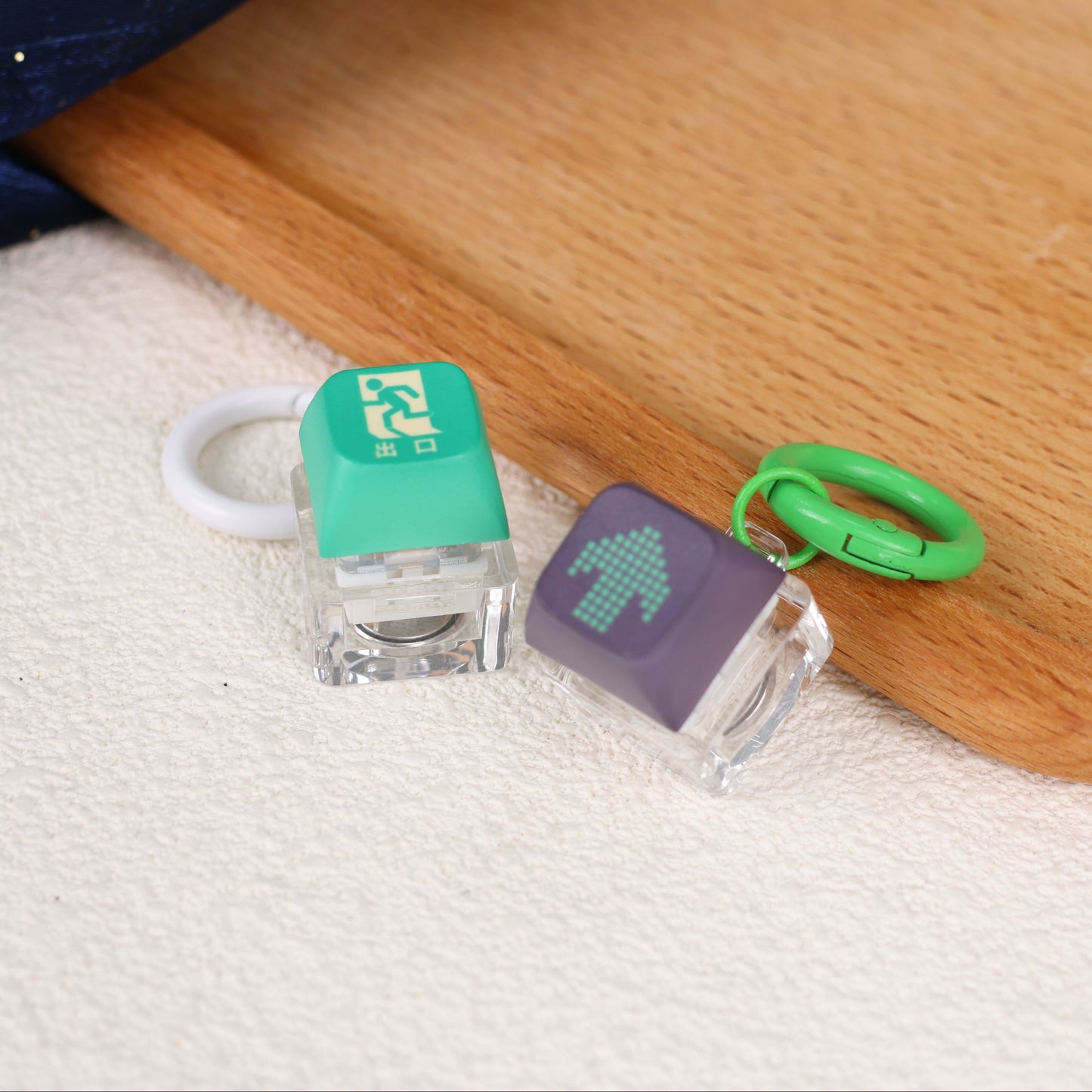Two small electronic devices with green and black keycaps on a wooden surface.