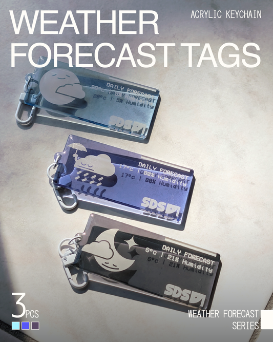 Three acrylic keychains with metal keyrings, shown on a light textured background. The keychains are translucent blue, purple, and dark gray/black, each printed with a weather icon and text including 'DAILY FORECAST', 'SDSD', and temperature/humidity readings.
